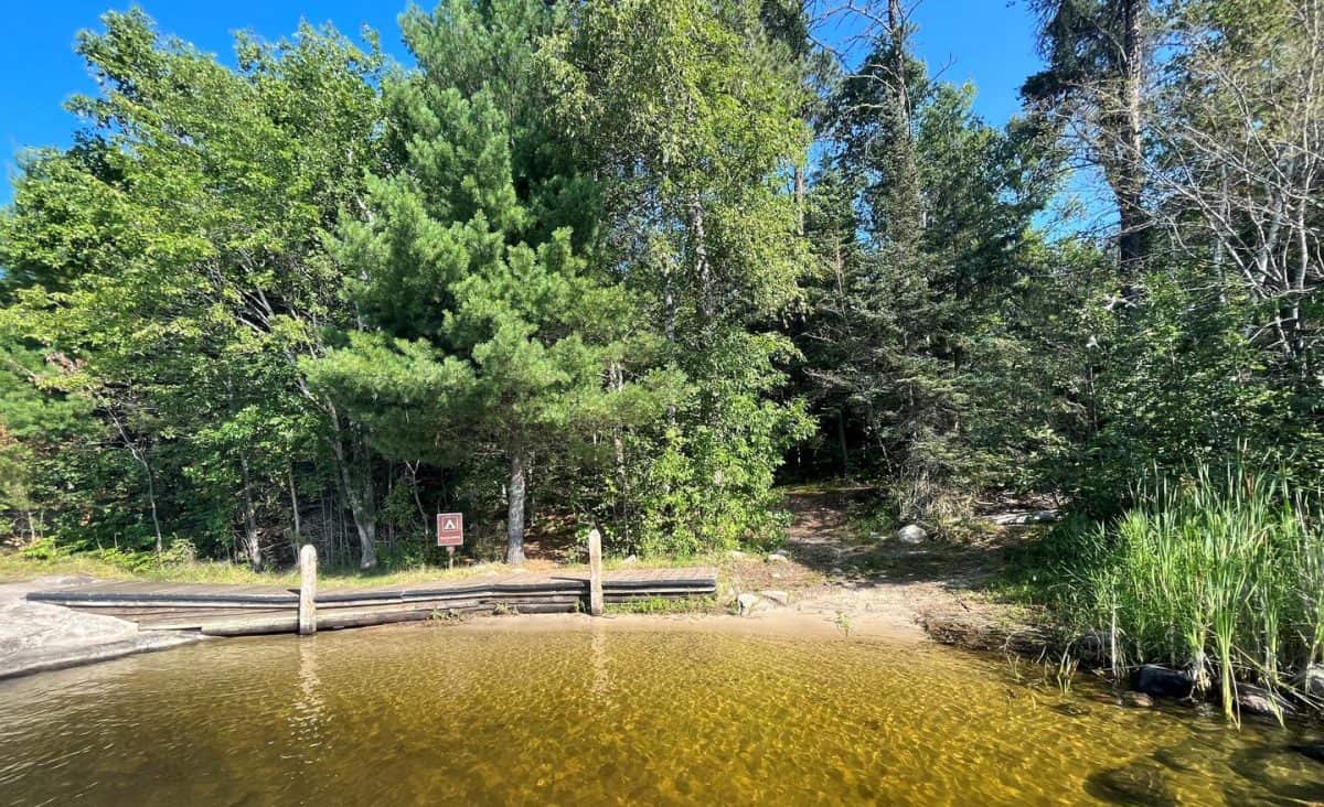 K1 View of sand landing at campsite with a board walk on shore with a couple of mooring posts and the campsite sign.