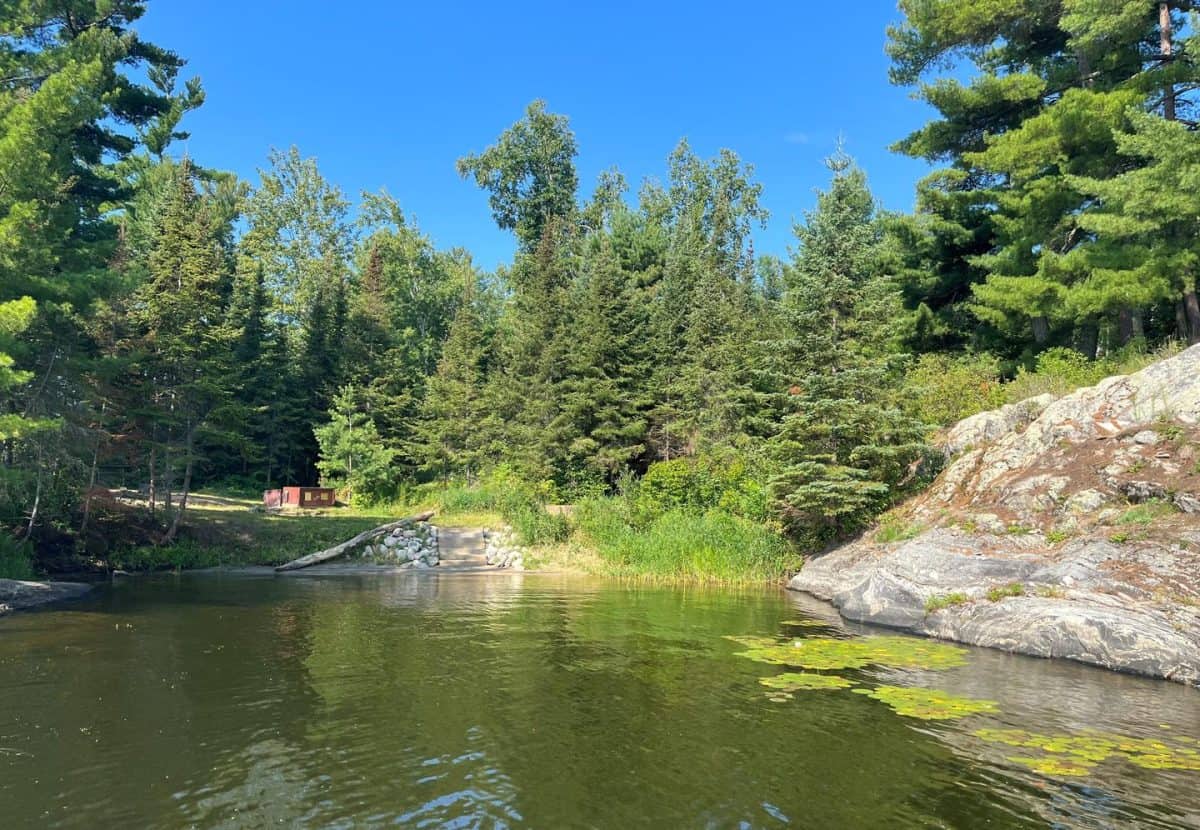 K7 View of sand landing from water with stairs leading down to the shoreline and a big log with the campsite in the background.