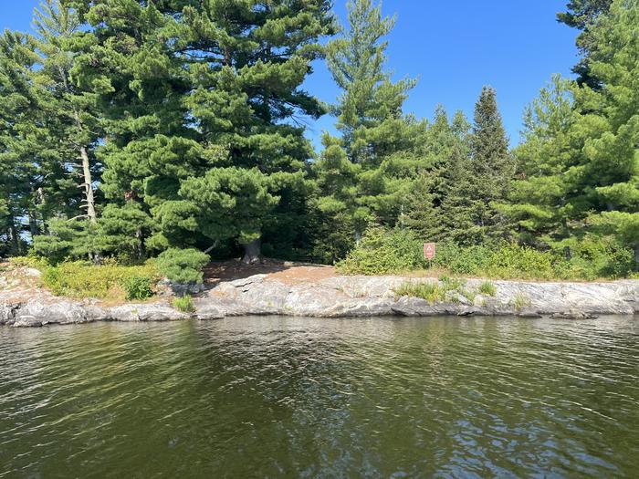 K7 View of campsite from water with the campsite sign on the rocky shoreline and the picnic table in the background.