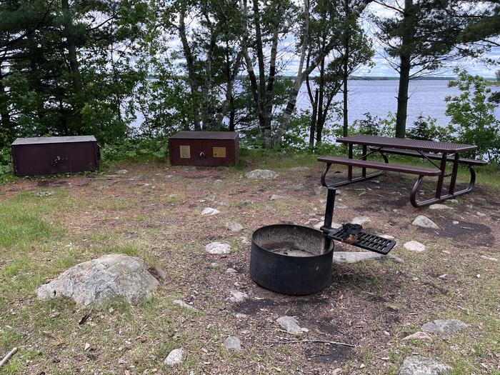 K11 Happy Landing view looking out from campsite of the fire ring picnic table and bear lockers with the water in site through the trees.