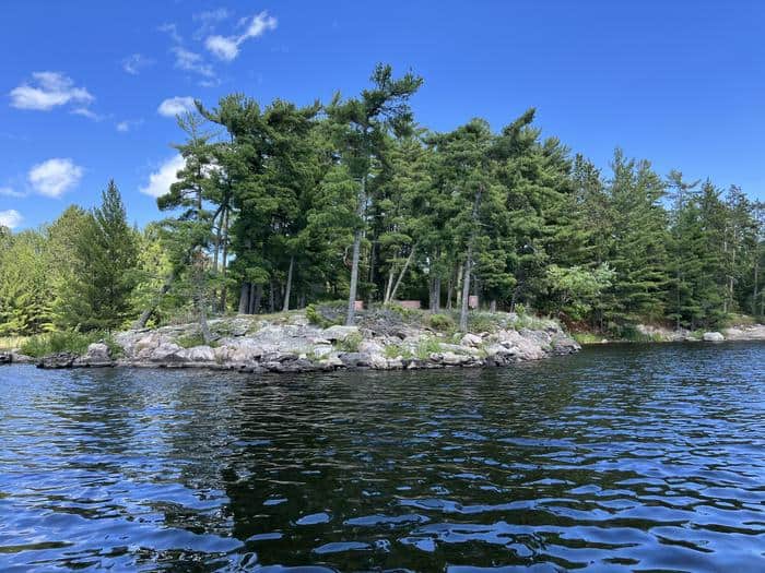 K17 Campsite from water with the campsite sign on rock and brown bear lockers at site.